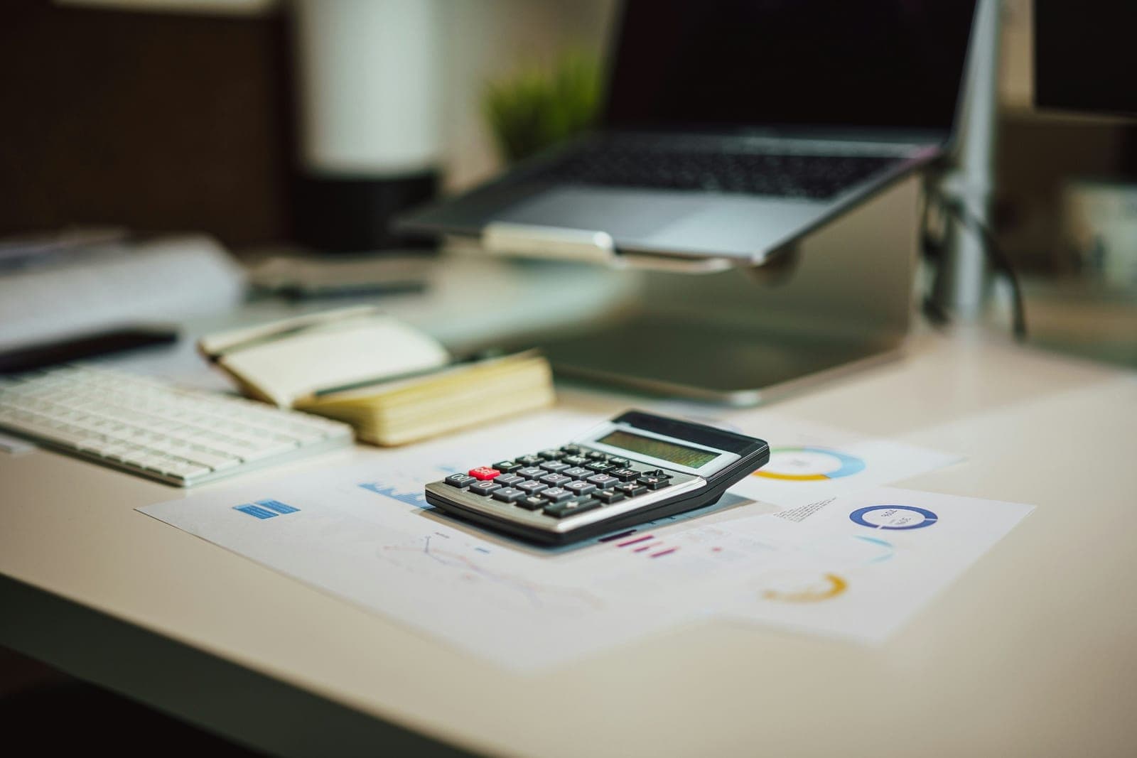 Calculator resting on printed financial reports beside a laptop on an accountant’s desk