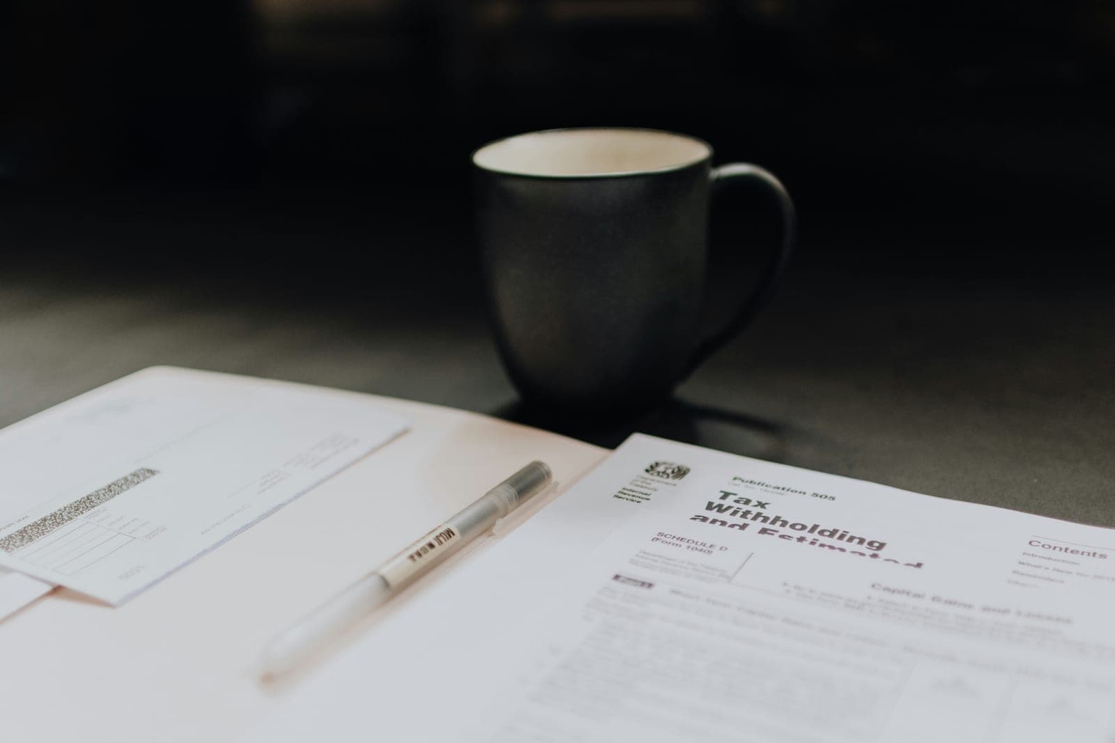 IRS tax forms and a pen on a desk beside a cup of coffee