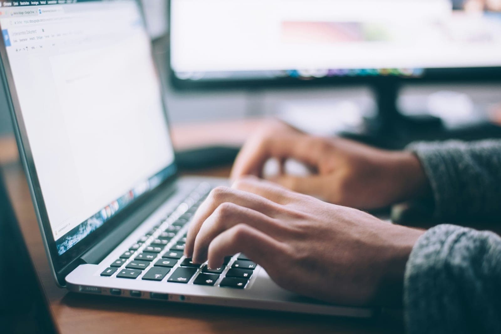 Hands typing on a laptop while working on a document at a desk