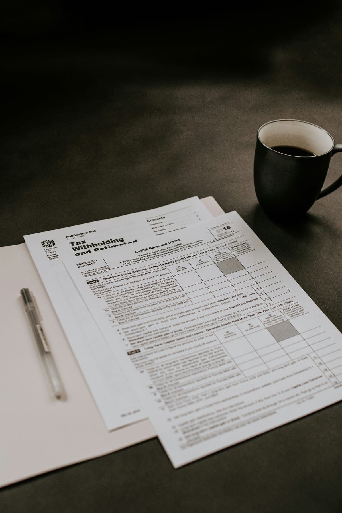 IRS Publication 505 tax withholding forms and Schedule D laid out in a folder with a pen